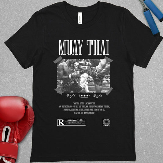 Black shirt with a design that has a picture of two Muay Thai fighters fighting each other. Below the picture is the words Fight Night and the phrase - Martial arts is like a mountain, you see the top, and you hike and you climb, and you finally reach the peak, and you realize it was a false summit, and in front of you lies an entire new mountain range.