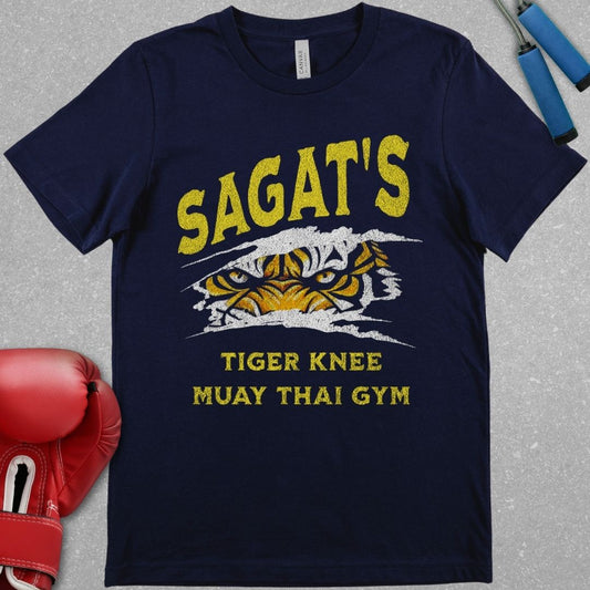 Navy shirt with a design that says Sagat’s Tiger Knee Muay Thai gym and there is a picture of a tiger’s eyes