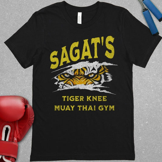 Black shirt with a design that says Sagat’s Tiger Knee Muay Thai gym and there is a picture of a tiger’s eyes