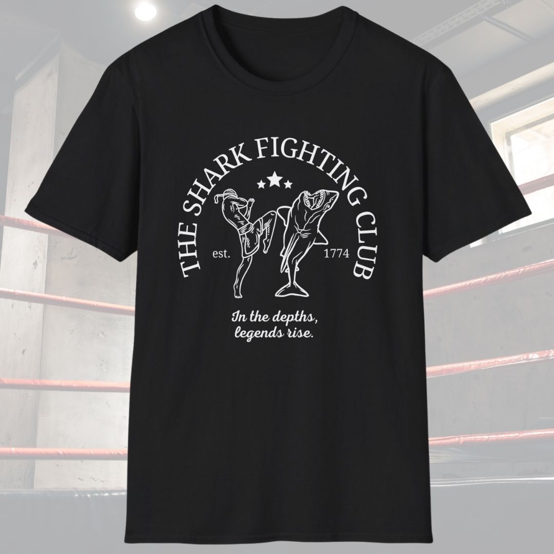 Black shirt with the slogan The Shark Fighting Club. It has a picture of a Muay Thai Fighter throwing a knee at the shark with the phrase In the depths, legends will rise.