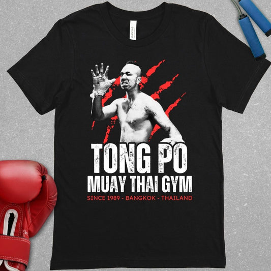 Black shirt with a picture of Tong Po and the design has the words Tong Po Muay Thai gym – Since 1989, Bangkok, Thailand. 