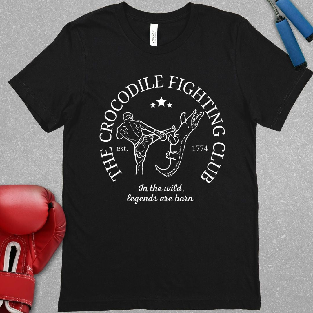 Black shirt with a white design. The design has the words The Crocodile Fighting Club and has a Muay Thai guy throwing a kick to a crocodile's head. At the bottom of the design has the words In the wild, legends are born.