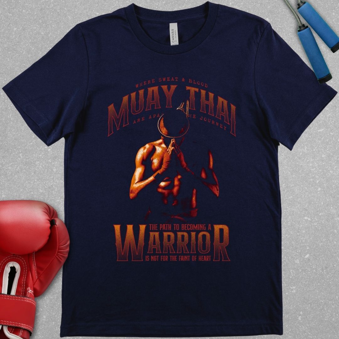 Navy shirt with a red design. The design features a Muay Thai fighter wearing the Mongkhon and bowing his head with his hands in prayer. The top of the shirt features the words Muay Thai and the phrase - Where sweat and blood are a part of the journey. The bottom of the shirt features the phrase - the path to becoming a warrior is not for the faint of heart.